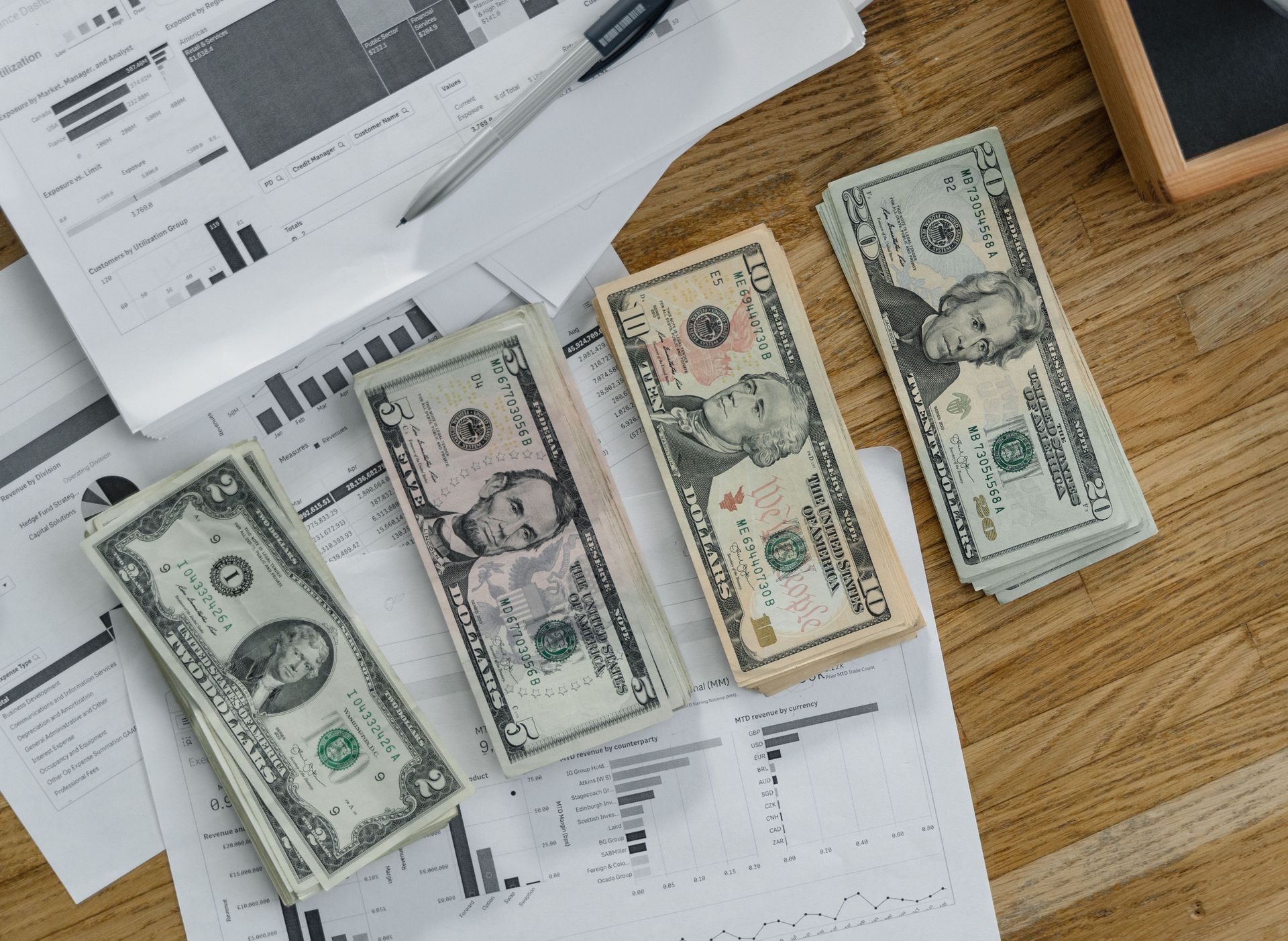 Stacks of US Dollar banknotes placed over financial documents and reports on a desk.